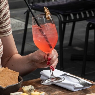 Hand holding an orange spritz next to a plate of lavosh.