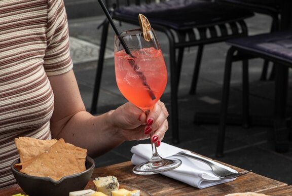 Hand holding an orange spritz next to a plate of lavosh.