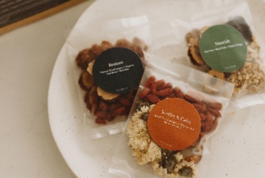 A white plate with three small plastic bags with different herbal tea fillings. 