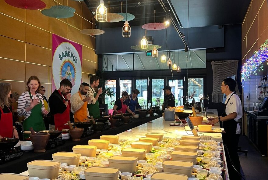 Side view of people participating in a cooking class with a chef standing up front. 