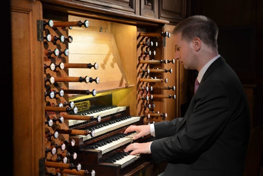 A man in profile playing a grand organ. 