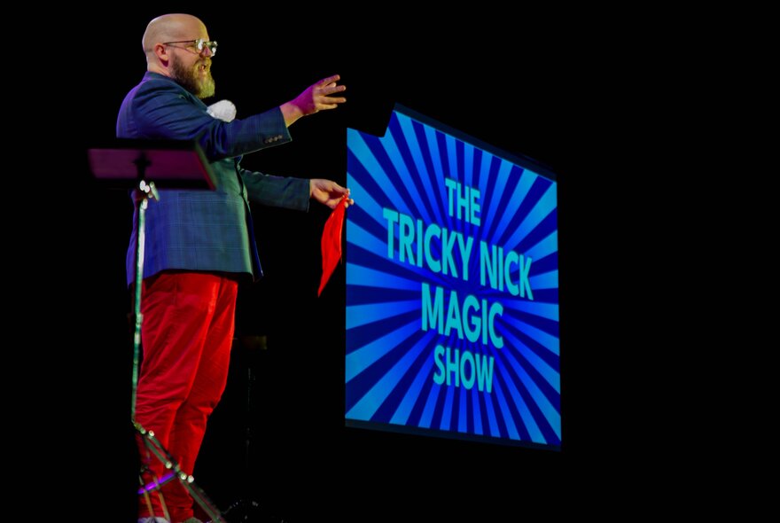 Magician performing on stage holding a red handkerchief.