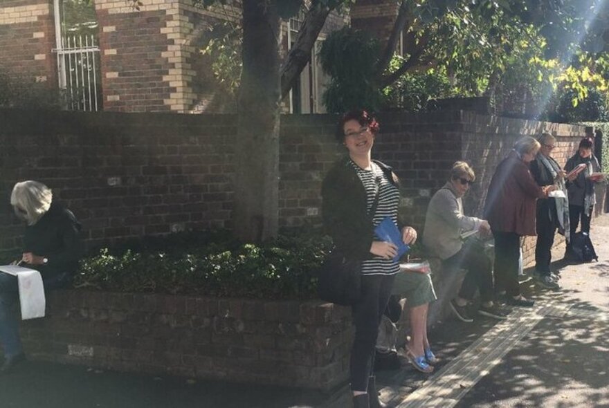 People sitting on a streetside wall, sketching in dappled sunlight.