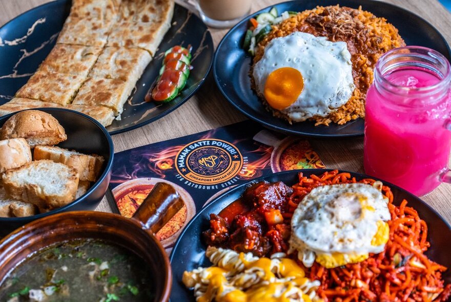 A spread of colourful rice dishes, roti, curry and a pink drink.