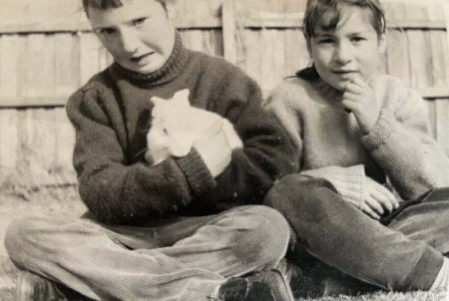 Family photograph of a young boy and girl, the boy holding a white rabbit and making a face.