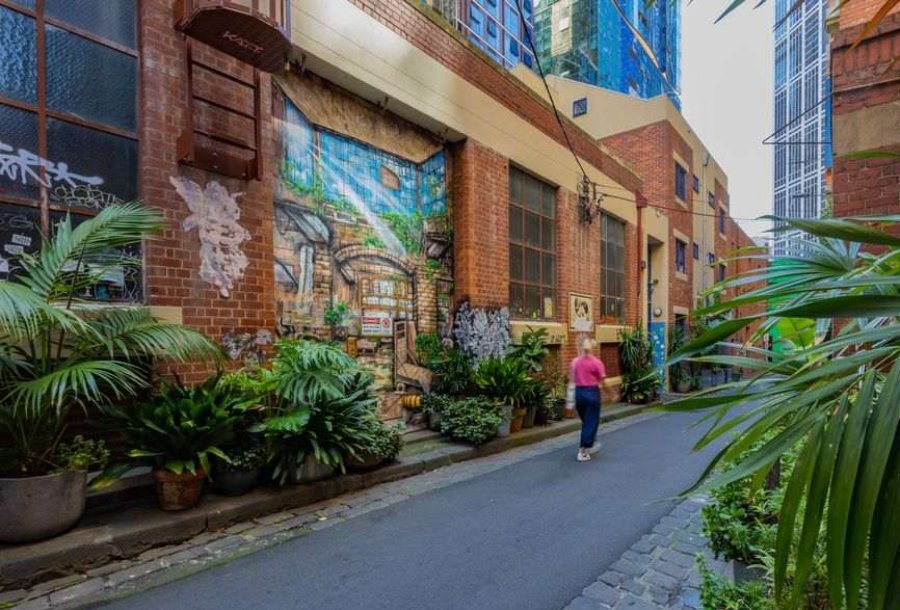 A woman in a pink jumper walking past a street art mural in a leafy laneway.