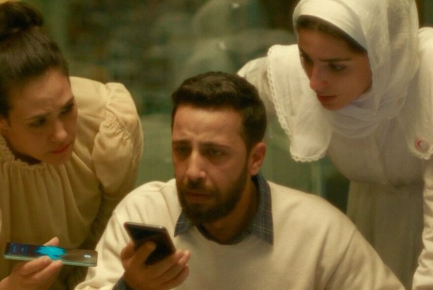 A man and two women speaking into a mobile phone, looking concerned.