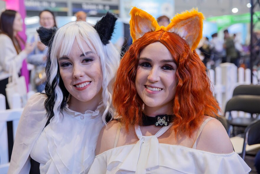 Two women with cat ears on smiling at an expo.