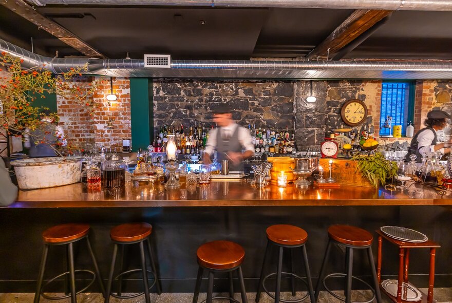 A bartender in a blur behind a cosy bar with barstools in a row, one pulled out. 