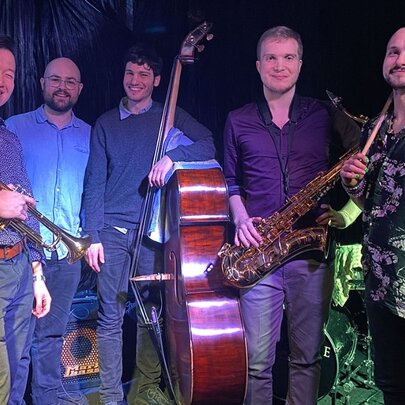 A jazz band lined up for a group shot, some holding instruments including a double bass, trumpet and saxophone. 
