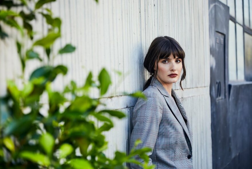 A model posing against a wall in a grey checked blazer.