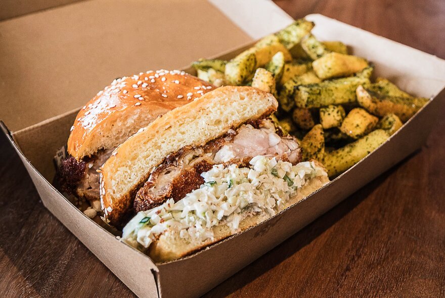 A takeaway meal in a cardboard container, which includes a large toasted sandwich and a side of seasoned fries.