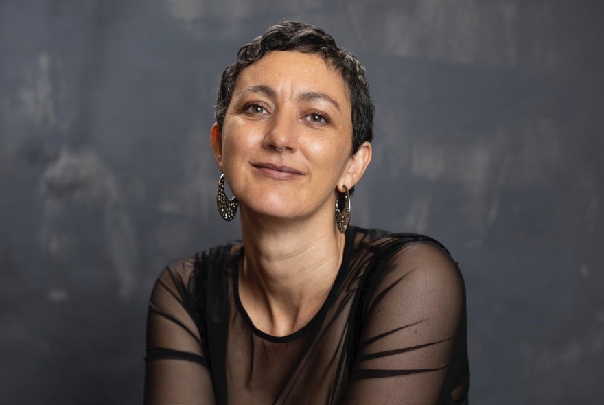 Dr Mykaela Saunders, wearing a black dress with transparent sleeves, short hair and earrings.