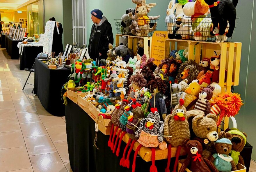 A person standing at a stall of various crafted stuffed toys. 