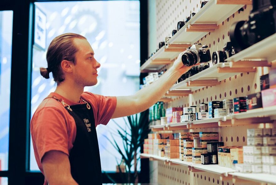 Storekeeper filling shelves of cameras and film in a camera store.