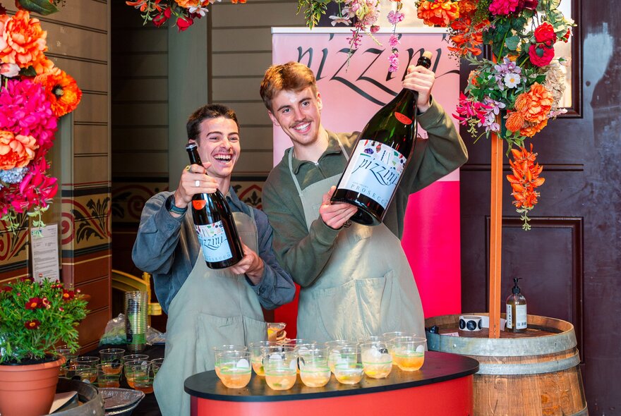 Market stallholders holding bottles of Prosecco in front of rows of glasses.
