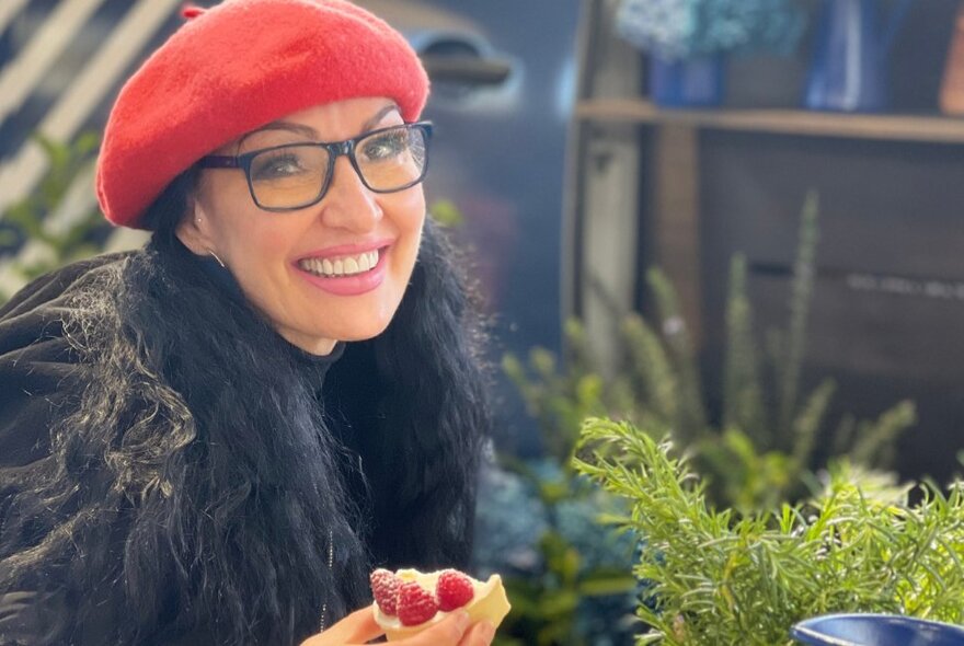 A smiling woman wearing a red beret, and holding food in her hand.