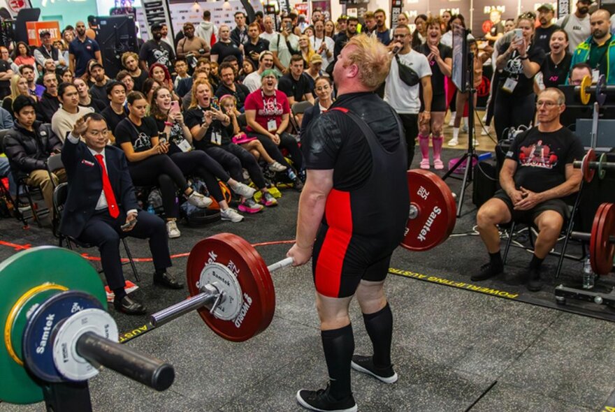 A crowd of seated people watching a weightlifter lift weights.