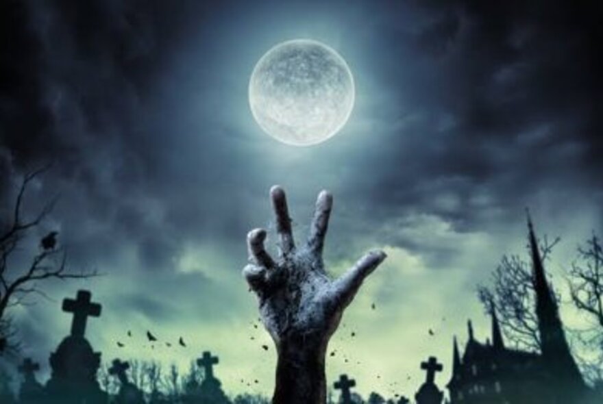 A zombie like decomposing hand rising up from a cemetery against the backdrop of a full moon and gravestones.