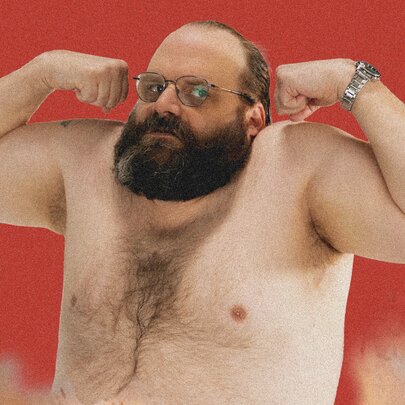 Comedian Greg Larsen, doing a bicep curl while shirtless in front of a red background.