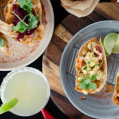 Two plates of tacos and a margherita cocktail, seen from above.