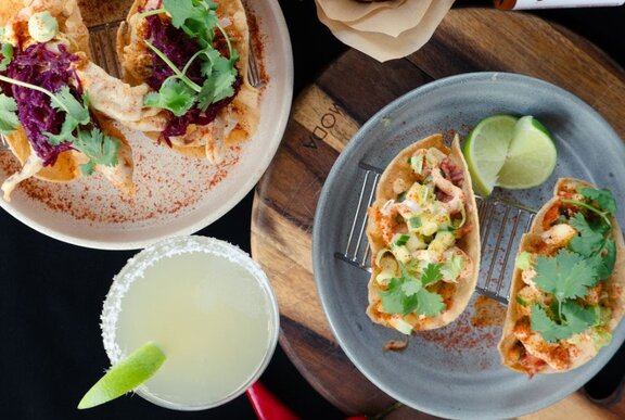 Two plates of tacos and a margherita cocktail, seen from above.
