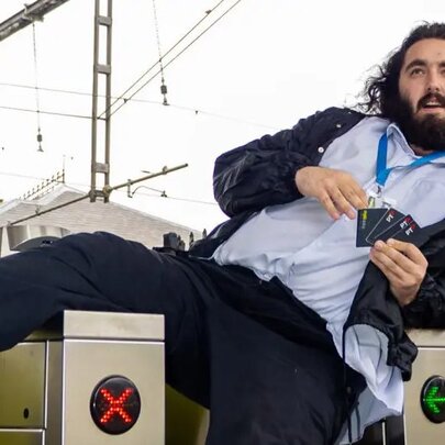 A bearded man dressed as a ticket inspection lounging over the gates of a station and holding Myki cards.