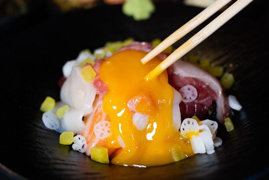 Chopsticks over a bowl of food with runny egg.
