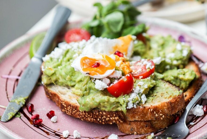 Pink plate with avocado on toast with poached eggs.