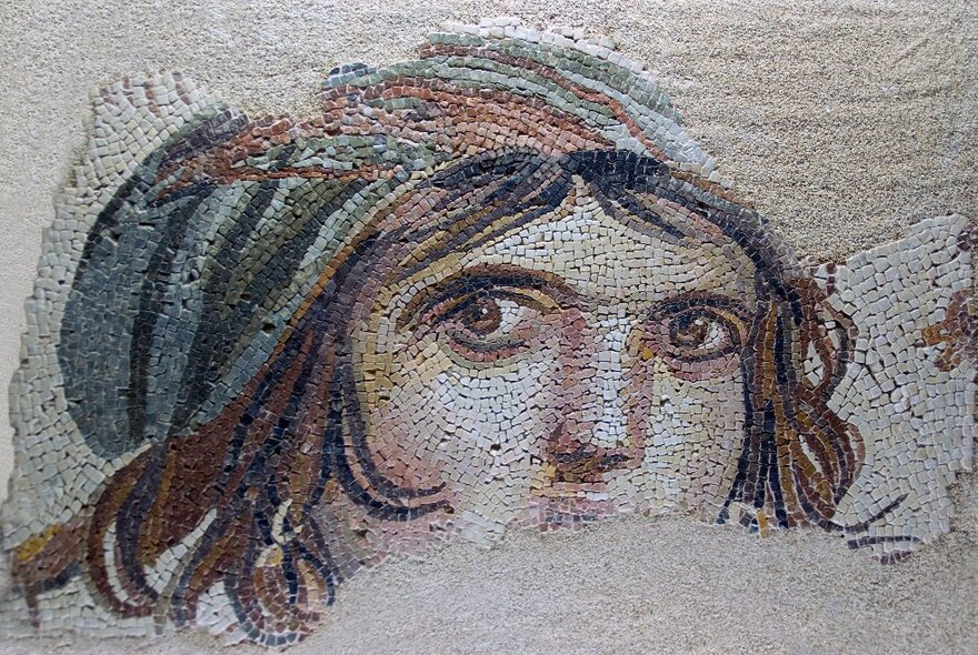 Detail from an ancient Roman mosaic of a face, with hair visible underneath a scarf.