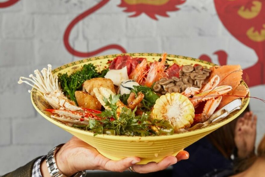 A bowl of hot pot with lots of fresh vegetables and meat on top.