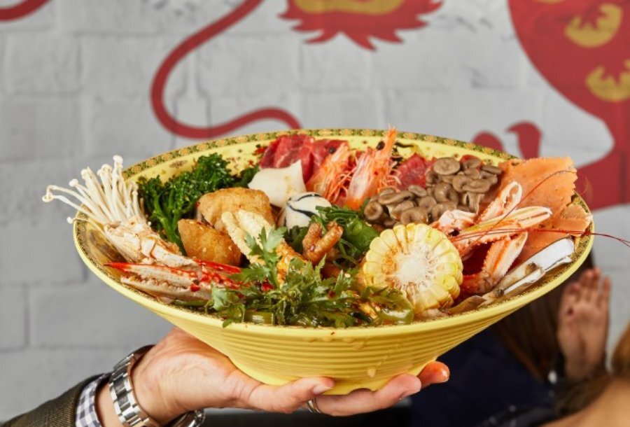 A bowl of hot pot with lots of fresh vegetables and meat on top.