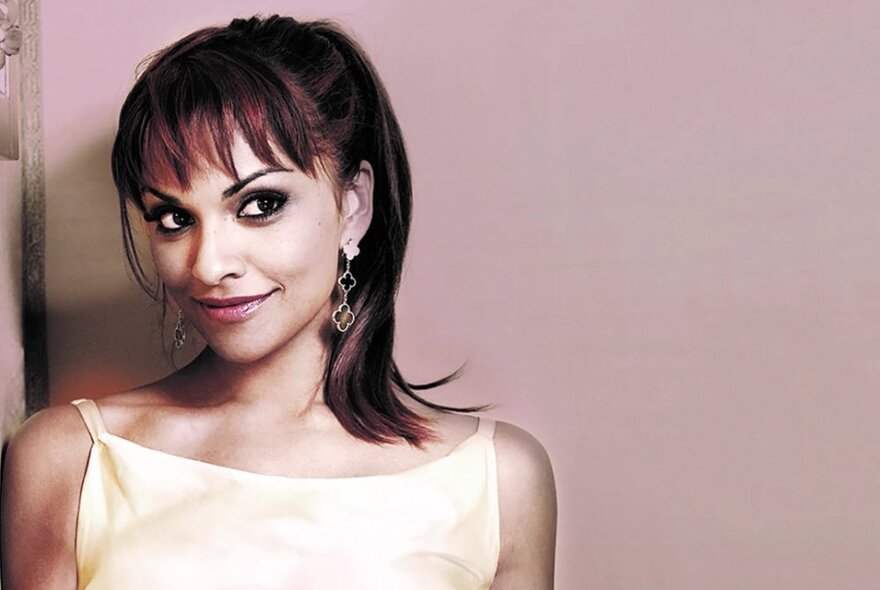 Portrait of opera sensation, Danielle De Niese, wearing a cream silk camisole and her brown hair in a ponytail.