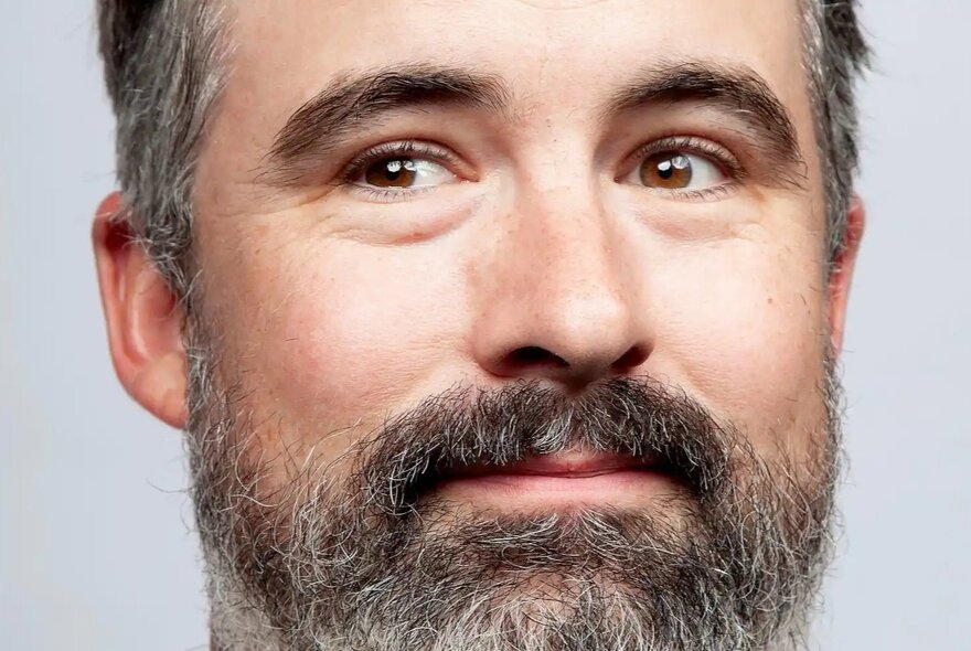 A close-up portrait of a man, Stuart Daulman, with a beard and graying hair looking off to the side.