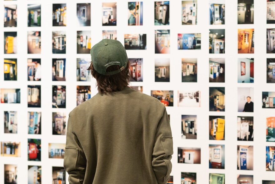 A person looking at a wall of photographs on display in a gallery space.