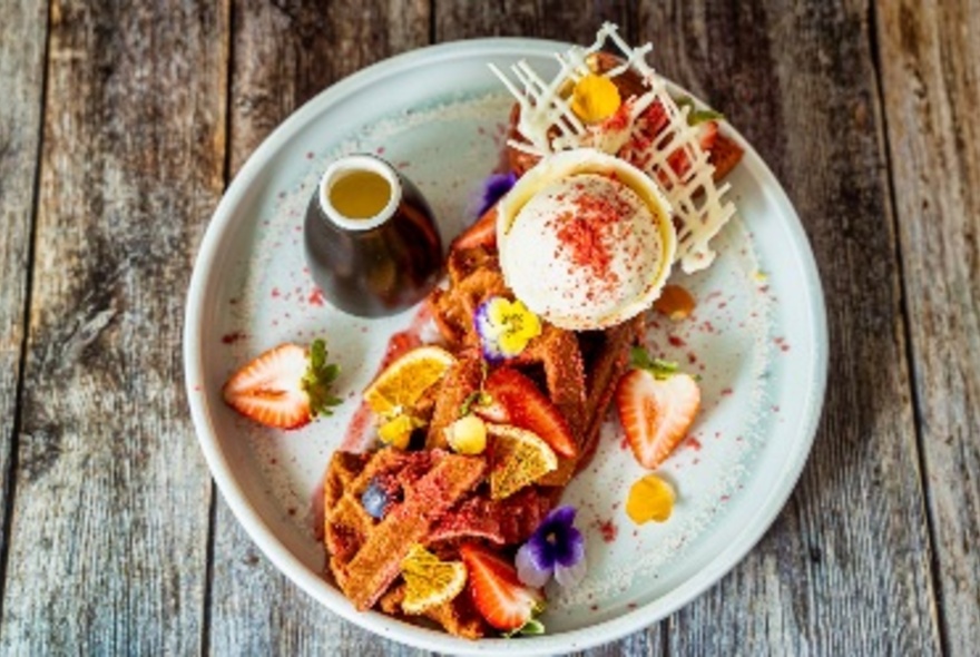 A dessert plate of waffles, fruit, ice cream and small jug of syrup.