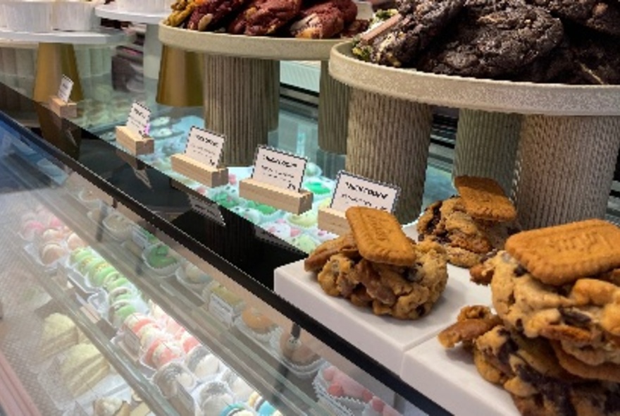 A cabinet full of small, delicious cakes with plates of biscuits on top. 