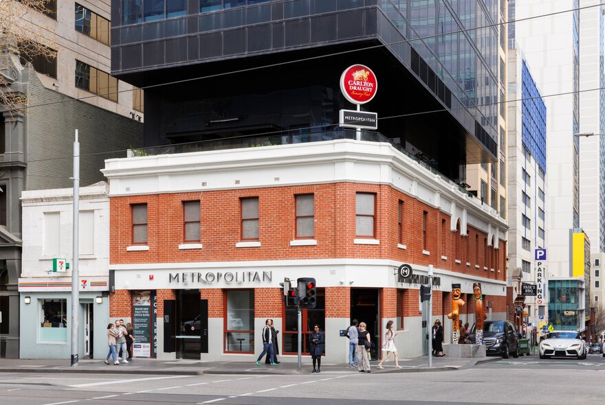 The exterior of the Metropolitan Hotel with people waiting to cross the road and a large city building in the background. 