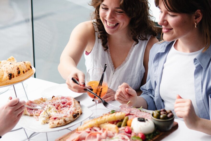 Two people smiling and seated at a table with dishes of food in front of them.