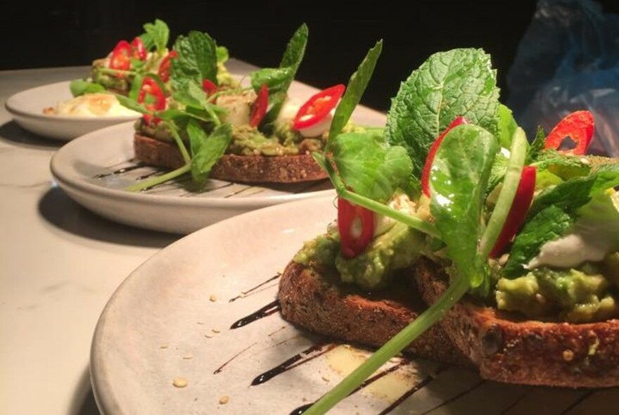 Three white plates of avocado on toast.