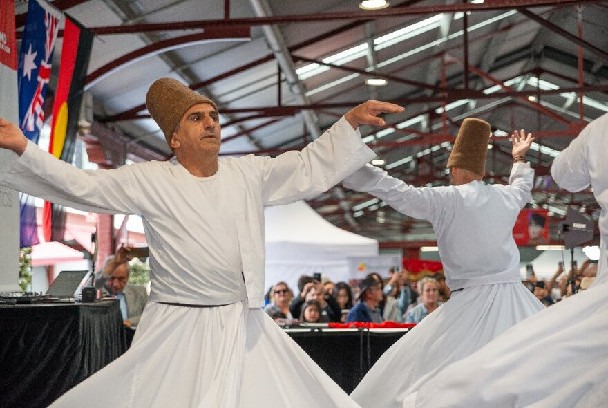 Whirling dervishes, men in white cloaks and brown fez hats spinning in an open space at Queen Victoria Market as part of the Turkish Pazar Festival.