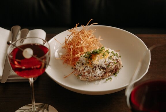 A restaurant dish beautifully presented next to a wine and cocktail.