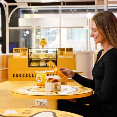 A woman sitting at a table and smiling while looking at the menu in the Gudetama cafe.
