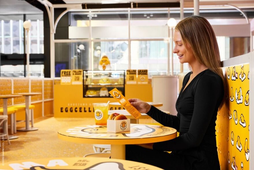A woman sitting at a table and smiling while looking at the menu in the Gudetama cafe.