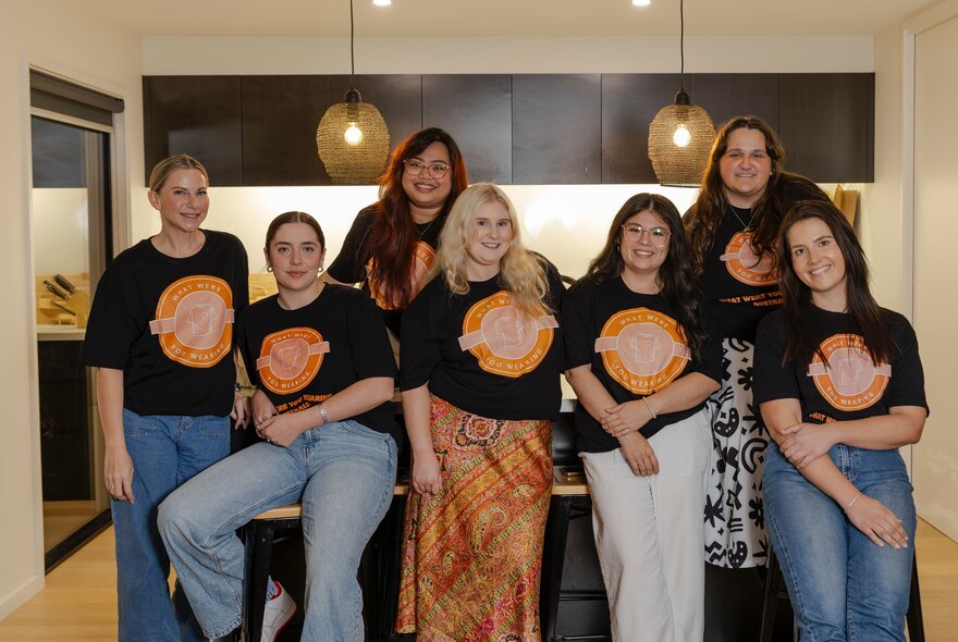 A group of people standing and sitting on stools in a kitchen setting.