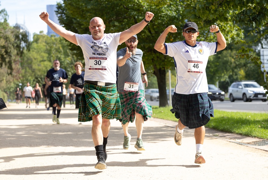 Three men running in kilts during a charity fun run.