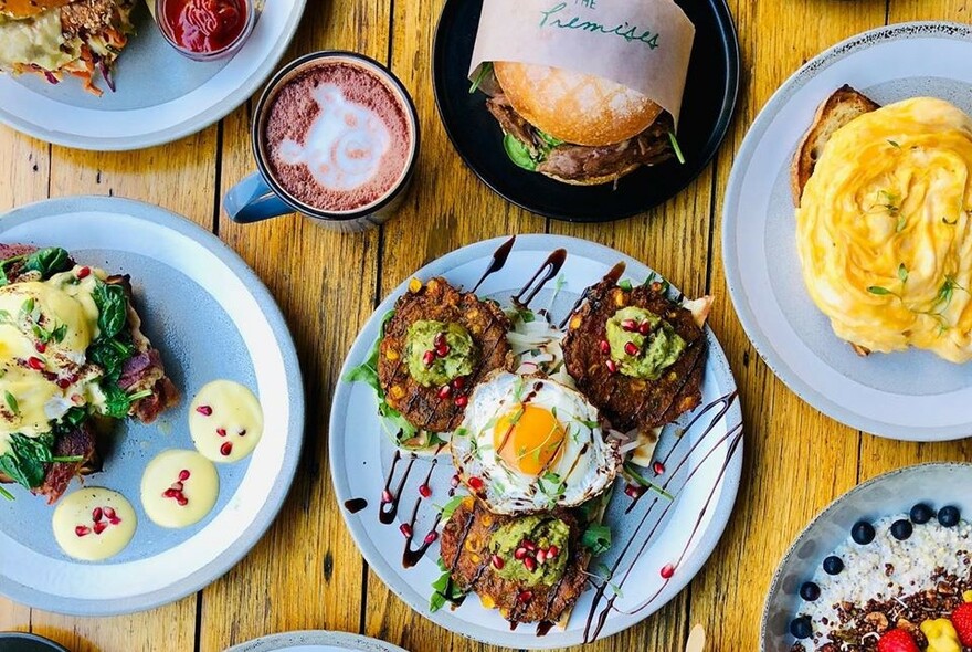 Array of food on plates including cooked eggs, sweetcorn fritters and a hamburger.