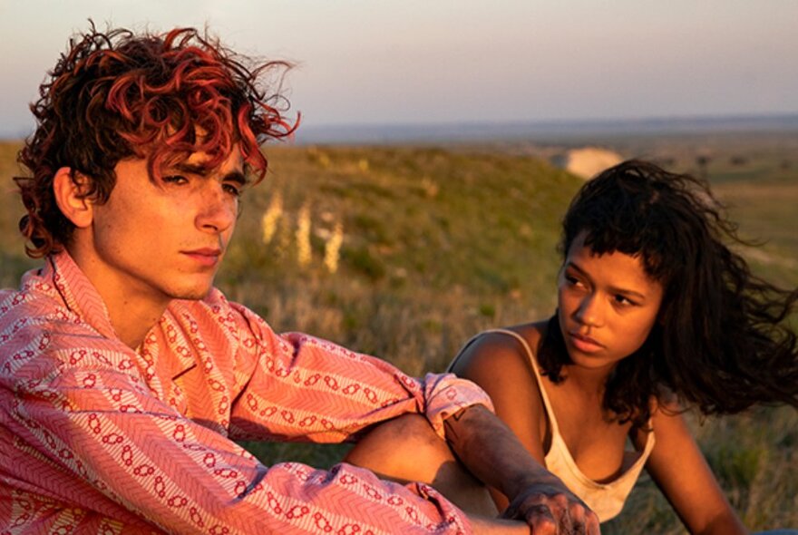Actor Timothée Chalamet and actor in a sun-drenched clifftop landscape. 