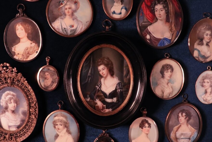 A collection of small, oval-framed portraits of regency-era women hanging together on a dark blue wall.