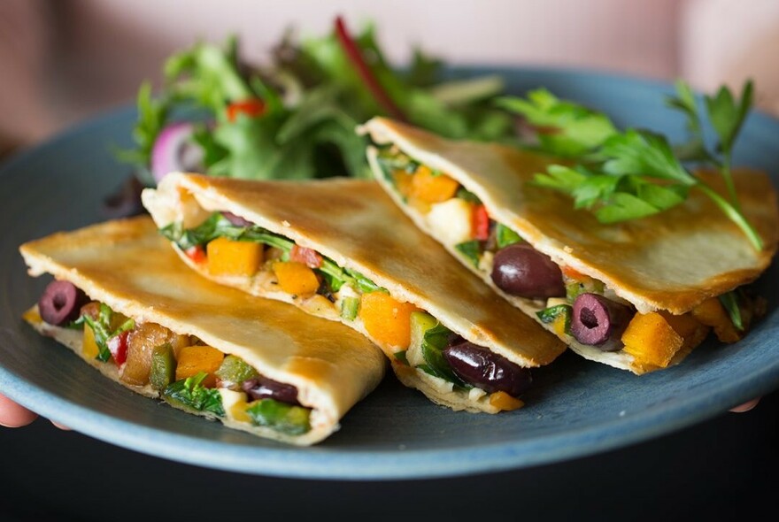 Plate with three slices of toasted panini filled with olives and vegetables.